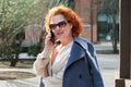 Attractive red-haired woman in an oversized shirt and a blue coat is talking on a mobile phone Royalty Free Stock Photo