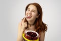 An attractive red-haired young woman holds a cake in her hand and licks a pastry cream off her finger