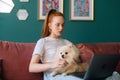 Attractive redhead young woman having online video call using laptop computer sitting on comfortable sofa cuddling cute Royalty Free Stock Photo