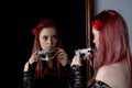 Attractive redhead young woman is looking at herself in the mirror holding a carnival mask Royalty Free Stock Photo
