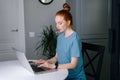 Attractive redhead young woman working typing on laptop computer sitting at table in living room. Royalty Free Stock Photo