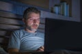 Attractive and relaxed internet addict man networking concentrated late at night on bed with laptop computer in social media Royalty Free Stock Photo