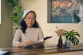 Attractive and relaxed 60s mature Asian woman reading a book at a table in her living room Royalty Free Stock Photo