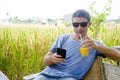 Attractive 30s Caucasian man smiling happy and relaxed sitting at rice field coffee shop in Asia holiday trip using internet on mo