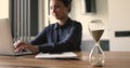 Indian businesswoman work on laptop, hourglass showing passage of time