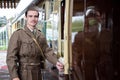 Handsome and sad male British soldier in WW2 vintage uniform at train station next to locomotive train.