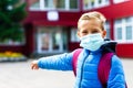 Attractive schoolboy in protective mask standing outdoor excited child points finger at school close up Royalty Free Stock Photo