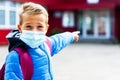 Attractive schoolboy in protective mask standing outdoor excited child points finger at school close up Royalty Free Stock Photo
