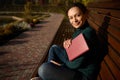 Attractive self-confident woman in casual denim rests in a park sitting in lotus position on a wooden bench with a book in her