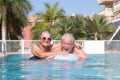 Attractive senior couple floating in the swimming pool playing with inflatable mattress. Happy retired people enjoying summer