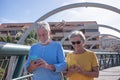 Attractive senior couple walking on a bridge in the city. Looking at their own mobile phone and smiling. Elderly modern and