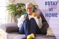 Attractive senior lady sitting on sofa at home using her smart phone for chatting with friends or family drinking a coffee cup - Royalty Free Stock Photo