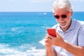 Attractive senior man in sea vacation, using phone and smiling. Blue sea and horizon over water