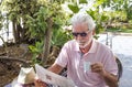 Attractive senior man with sunglasses sitting at the coffee table while reading the newspaper and drinking a coffee cup - around Royalty Free Stock Photo