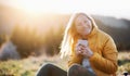 Attractive senior woman sitting outdoors in nature at sunset, relaxing with coffee. Royalty Free Stock Photo