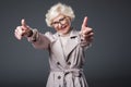 attractive senior woman in trench coat and eyeglasses showing thumbs up,