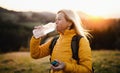 Attractive senior woman walking outdoors in nature at sunset, drinking water. Royalty Free Stock Photo