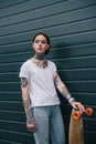 attractive serious tattooed girl standing with skateboard against black