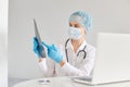 Attractive serious woman doctor sitting at table and working on laptop computer, having online conference with colleagues, showing Royalty Free Stock Photo