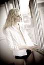 Attractive blonde with white shirt looking on the window in daylight. Portrait of sensual long fair hair woman wearing blouse Royalty Free Stock Photo