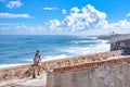 Attractive sexy Hispanic male sitting on a parapet wall having a beautiful wavy seascape behind