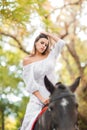 Horseback riding. Beautiful young woman in a white dress riding on a brown horse outdoors. Royalty Free Stock Photo