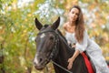 Horseback riding. Beautiful young woman in a white dress riding on a brown horse outdoors. Royalty Free Stock Photo