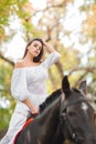 Horseback riding. Beautiful young woman in a white dress riding on a brown horse outdoors. Royalty Free Stock Photo