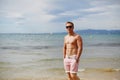 Attractive shirtless athletic young man on the beach by the sea. Young muscular man with perfect body in shorts and Royalty Free Stock Photo
