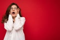 Attractive shocked amazed surprised young curly brunette woman wearing white shirt and optical glasses isolated on red Royalty Free Stock Photo