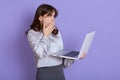 Attractive shocked businesswoman with laptop in hands posing isolated over lilac background, wearing elegant attire, has Royalty Free Stock Photo