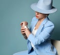 Attractive short haired brunette woman in blue business smart casual suit, hat sitting looking at watch