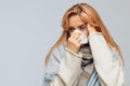 Sick young woman wrapped in warm scarf with napkin blowing nose,, having headache.Cold, flu Royalty Free Stock Photo