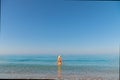 An attractive slender young Caucasian woman in a swimsuit and a straw hat stands waist-deep in sea water in the morning Royalty Free Stock Photo