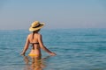 An attractive slender young Caucasian woman in a swimsuit and a straw hat stands waist-deep in sea water in the morning Royalty Free Stock Photo