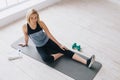 Attractive slim female doing stretching exercises on black mat in modern bright fitness center. Royalty Free Stock Photo