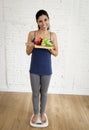 Attractive slim latin woman or teenager girl checking weight on scale holding vegetable tray Royalty Free Stock Photo