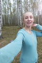 Attractive slim woman in a blue jumper takes a selfie in a birch forest Royalty Free Stock Photo