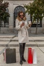 Attractive slim woman looks at her mobile phone while having a coffee in the street next to her shopping bags Royalty Free Stock Photo