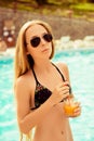 Attractive slim woman in swimsuit drinking juice near pool