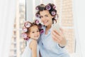 Attractive small kid with positive expression, charming smile stands near her mother, make selfie with modern mobile phone, pose a Royalty Free Stock Photo