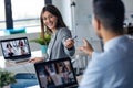 Attractive business woman leaves a pen to her partner while doing a video call with diverse colleagues with laptop in the office