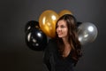 Attractive smart dressed woman with dark long hair holds colorful balloons behind her back, looks aside, celebrates new year,