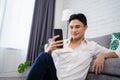 Attractive smart young man sitting on a floor in the living room, using mobile phone Royalty Free Stock Photo