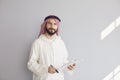 Attractive smiling arab man writes in clipboard on gray background