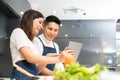 Attractive Smiling Asian couple cooking and using a digital tablet in a modern kitchen at home. Happy Young Man and beautiful Royalty Free Stock Photo