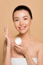 Attractive smiling asian girl holding glass container with moisturizing cream Royalty Free Stock Photo