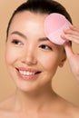 Attractive smiling asian girl using pink silicone cleansing facial brush