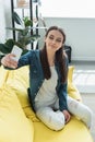 attractive smiling girl sitting on sofa and taking selfie Royalty Free Stock Photo