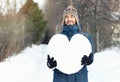 Attractive smiling man holding a huge heart made of snow in winter forest. Fall in love. Declarations of love, romantic feelings